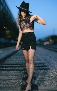 a woman in a black hat and skirt standing on railroad tracks